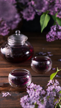 Purple tea is poured from a glass teapot into cups. Lilac flowers are all aroundの写真素材