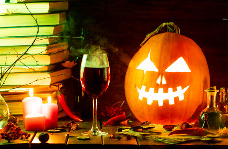 A pumpkin with a carved face glows on the table next to the booksの写真素材