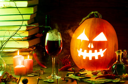 A pumpkin with a carved face glows on the table next to the booksの写真素材