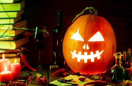 A pumpkin with a carved face glows on the table next to the booksの写真素材