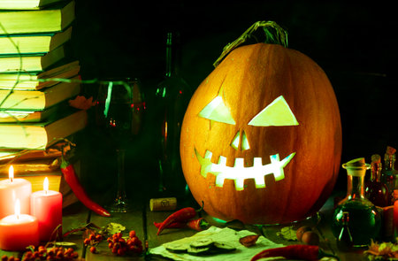 A pumpkin with a carved face glows on the table next to the booksの写真素材
