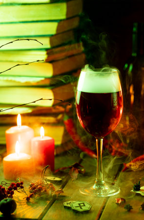 A glass of steaming wine on the table next to books and candlesの写真素材