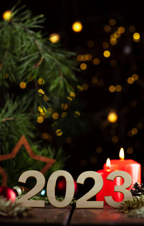 Wooden numbers 2023 on the table among spruce twigs and candles