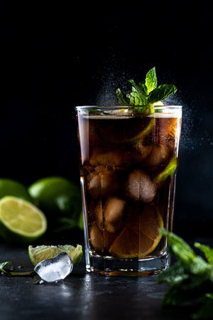 Cola is poured into a glass with ice and lime slicesの写真素材
