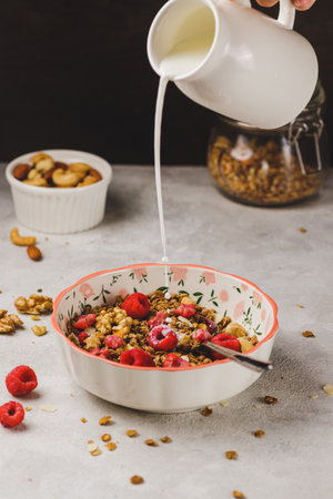 A plate with granola and raspberries, filled with milkの写真素材