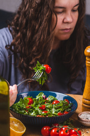A woman eats a salad of arugula and cherry tomatoesの写真素材