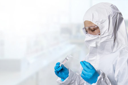Medical healthcare NHS technician holding COVID-19 swab collection kit, wearing white PPE protective...