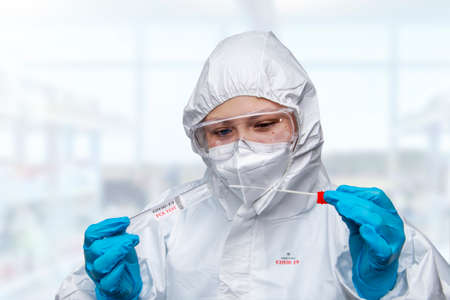 Medical healthcare NHS technician holding, COVID-19 swab collection kit, wearing white PPE protective suit mask gloves, test tube for taking OP NP patient specimen sample, PCR DNA testing protocol processの写真素材