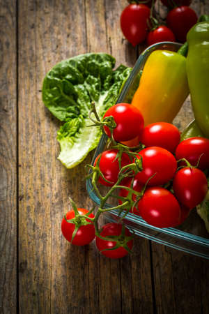 Bunch of vegetables in the glass jar. Red tomato, yellow pepper and green salad on wooden table.の写真素材