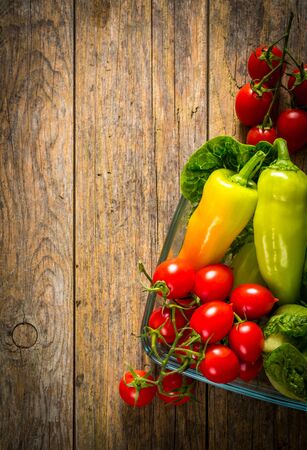 Bunch of vegetables in the glass jar. Red tomato, yellow pepper and green salad on wooden table.の写真素材