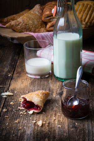 assorted breakfast pastries with jam and milk on old wooden tableの写真素材