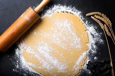 Rolling dough with wooden roller and flour on the black backgroundの写真素材