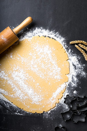 Rolling dough with wooden roller and flour on the black backgroundの写真素材
