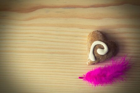gingerbread in the shape of a heart with decoration and pink featherの写真素材