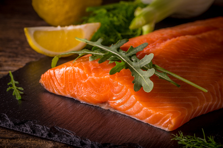 Salmon filet with lime, salt, pepper, rucoli,fennel and rosemary on black plate ready to cook.の写真素材
