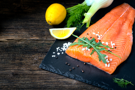 Salmon filet with lime, salt, pepper, rucoli,fennel and rosemary on black plate ready to cook.の写真素材
