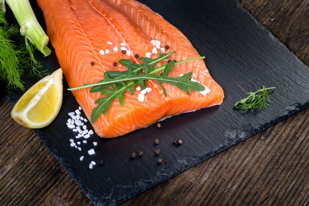 Salmon filet with lime, salt, pepper, rucoli,fennel and rosemary on black plate ready to cook.の写真素材