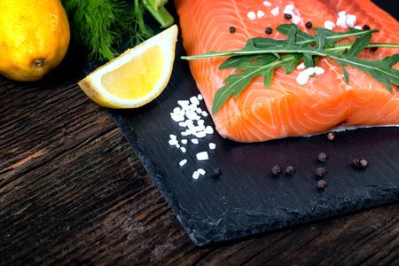 Salmon filet with lime, salt, pepper, rucoli,fennel and rosemary on black plate ready to cook.の写真素材
