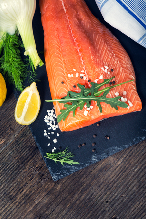 Salmon filet with lime, salt, pepper, rucoli,fennel and rosemary on black plate ready to cook.の写真素材