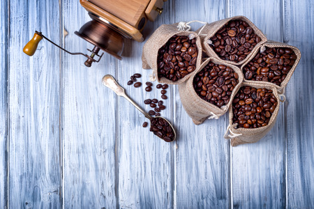 Coffee seeds in spoon with some jute bags filled with coffee and coffee grinderの写真素材