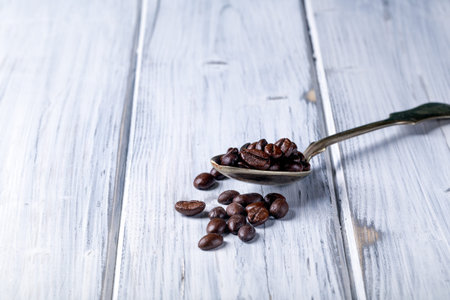 Silver spoon with coffee beans. White rural background. Brown coffeebeans.
