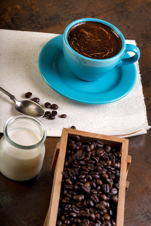 Cup of coffee and wooden containers filled with cofee beans on the rust background. Cane sugar. Low light.の写真素材