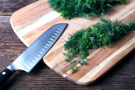 Sliced twig of dill on a wooden board with kknife. Branch seasoning aromatic spice.の写真素材