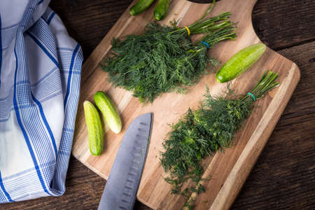 Sliced twig of dill on a wooden board with cucumber, knife and cloth. Branch seasoning aromatic spice.の写真素材