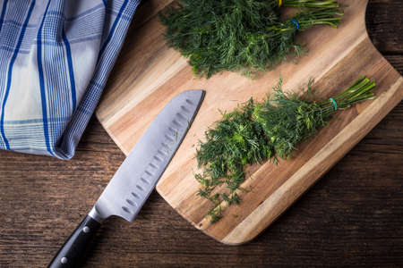 Sliced twig of dill on a wooden board with knife. Branch seasoning aromatic spice.の写真素材