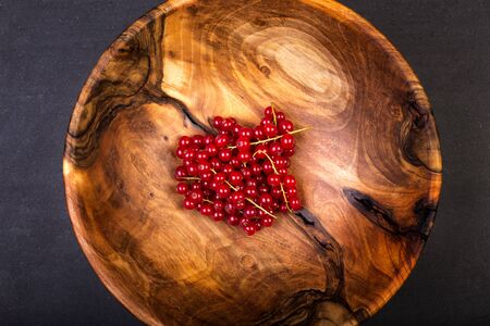 Bunch of red currants in a bowl from walnut wood. Healthy fruit with antioxidant.の写真素材