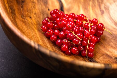 Bunch of red currants in a bowl from walnut wood. Healthy fruit with antioxidant.の写真素材