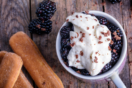 Cup of fresh natural blackberries with whipped cream and biscuits. Spoon and wooden table.の写真素材