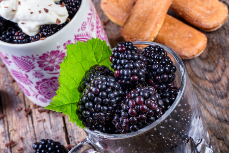 Cup of fresh natural blackberries with whipped cream and biscuits. Spoon and wooden table.の写真素材