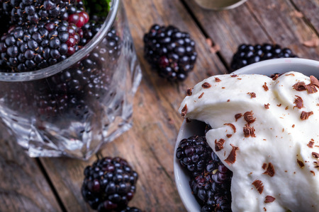 Cup of fresh natural blackberries with whipped cream. Spoon and wooden table.の写真素材
