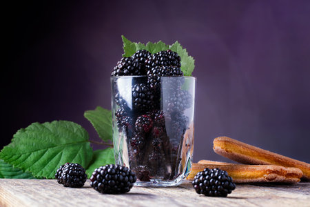 Cup of fresh natural blackberries with biscuits. Blackberries leaf. Spoon and wooden table.の写真素材