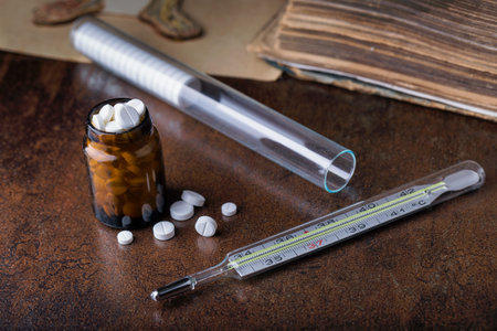 Bunch of blue pills with glass ampoules, thermometer and old medical book. Test-tube with...