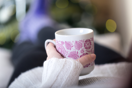 Woman holding hot chocolate in the mug with christmas tree in the background.の写真素材