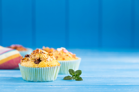 Fresh muffins with nuts and chocolate on the paper cupcake holder. Blue wooden rustic background.の写真素材