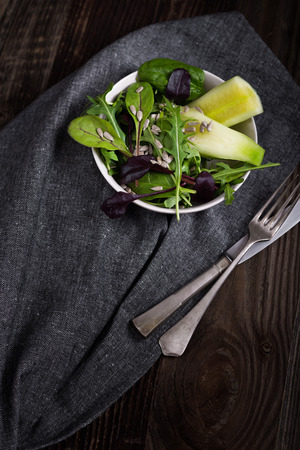 Spring salad with cucumber, arugula, sunflower seeds and olive oil in the white bowl.の写真素材