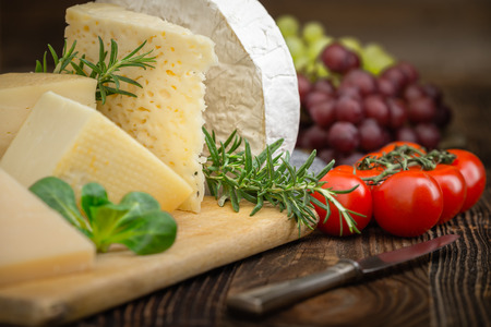 Bunch of fresh  high - quality cheeses from dairy with basil,rosemary, tomatoes and grapes.の写真素材