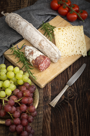 High - quality cheese with salame, grapes, tomatoes, rosemary on the wooden plate.の写真素材