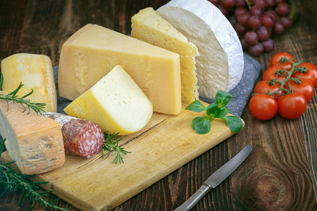 Bunch of fresh  high - quality cheeses from dairy with basil,rosemary, tomatoes, grapes and salame.の写真素材