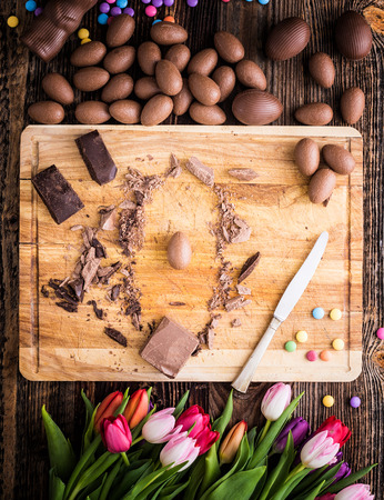 Chocolate eggs and raw pieces of chocolate with dragee and tulips.の写真素材