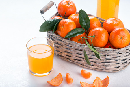 Full basket of mandarin with a glass of juice. Juicy tangerines with green leaves.の写真素材