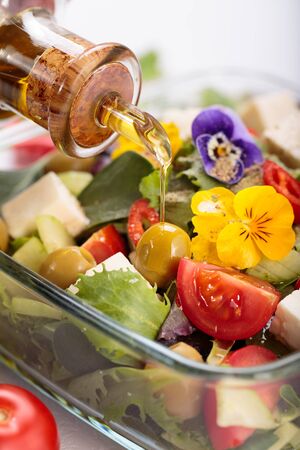 Bowl of vegetable salad with edible flowers and bottle of olive oil.の写真素材