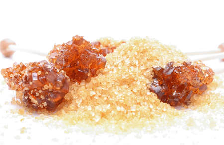 Brown sugar crystal on wooden stick and brown granulated sugar on a white backgroundの写真素材