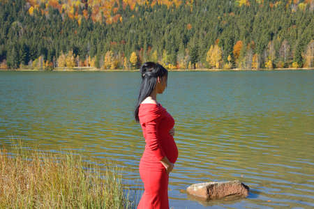 Beautiful young happy pregnant woman in fashion clothes in autumn sceneの写真素材