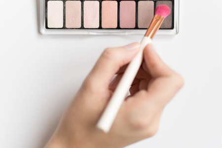 Hand holding a make up brush and eyeshadow on a white backgroundの写真素材