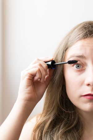 Young woman portrait putting on black mascara with natural lightの写真素材