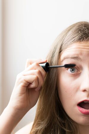 Young woman portrait putting on black mascara with natural lightの写真素材
